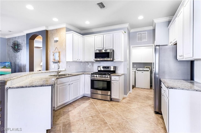 kitchen with appliances with stainless steel finishes, washer and dryer, white cabinets, and kitchen peninsula