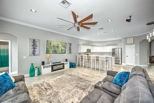 living room featuring ornamental molding, ceiling fan, and light wood-type flooring