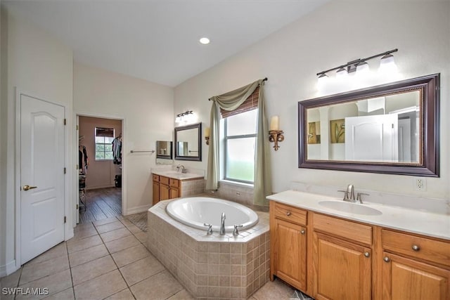 bathroom with tile patterned flooring, vanity, a wealth of natural light, and tiled tub