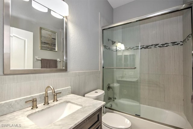 full bathroom featuring bath / shower combo with glass door, vanity, toilet, and tile walls