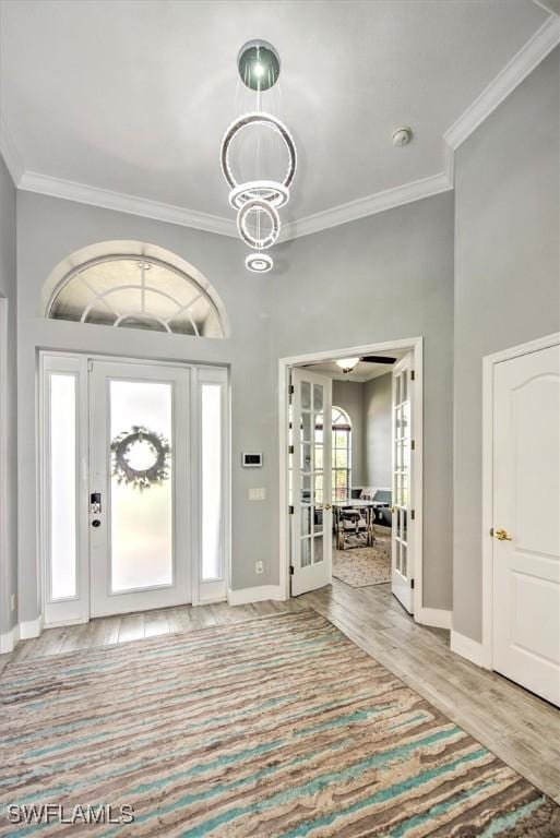 foyer entrance with a notable chandelier, crown molding, french doors, and light wood-type flooring