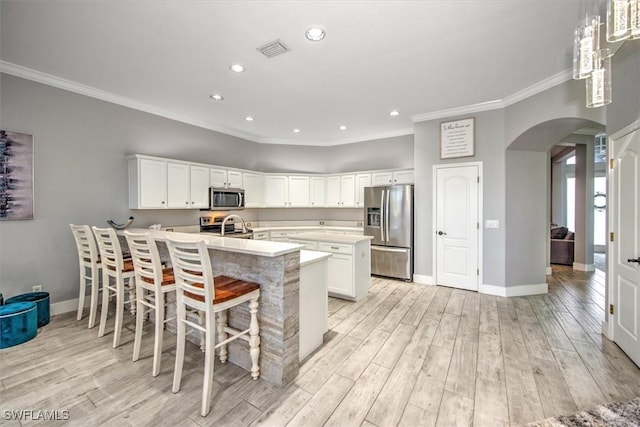 kitchen featuring stainless steel appliances, a breakfast bar, white cabinets, and light hardwood / wood-style flooring