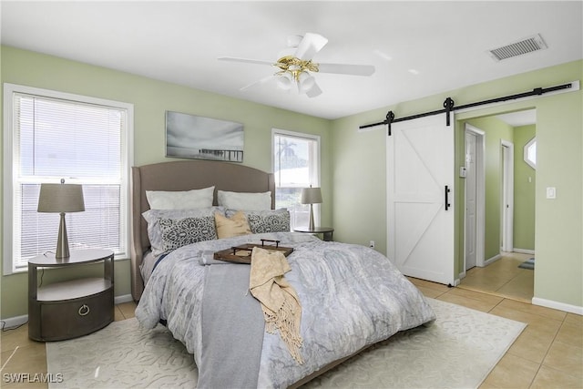 bedroom with ceiling fan, visible vents, a barn door, tile patterned floors, and baseboards
