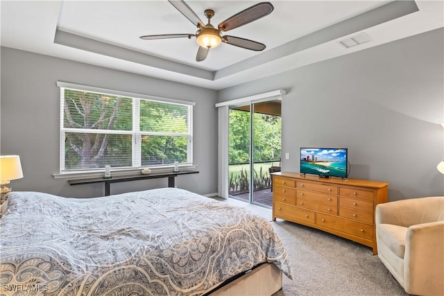 carpeted bedroom with ceiling fan, a tray ceiling, and access to outside