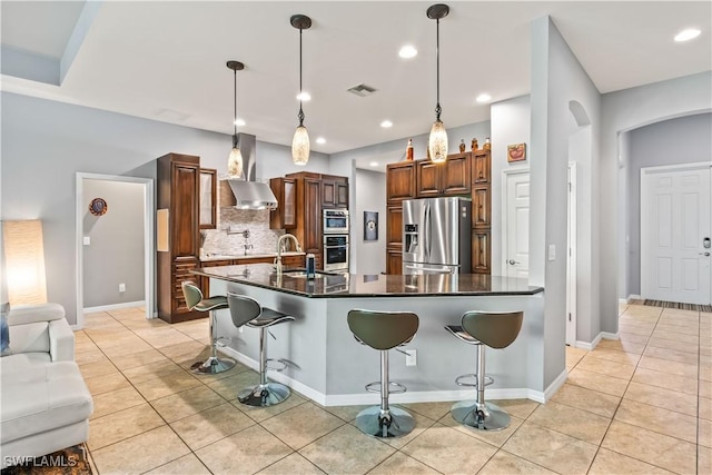 kitchen featuring appliances with stainless steel finishes, a kitchen breakfast bar, a spacious island, decorative light fixtures, and wall chimney exhaust hood