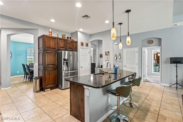 kitchen with stainless steel refrigerator with ice dispenser, light tile patterned flooring, sink, hanging light fixtures, and an island with sink