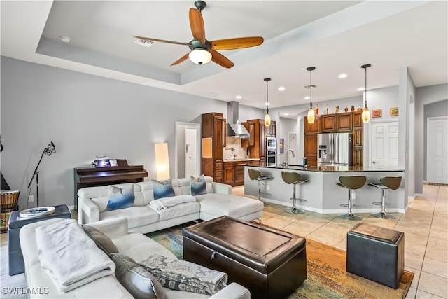 tiled living room featuring sink, ceiling fan, and a tray ceiling