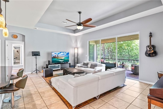 living room featuring a raised ceiling, light tile patterned flooring, and ceiling fan