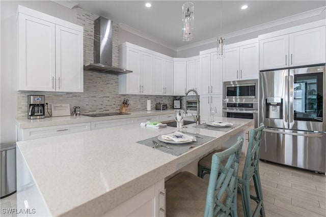 kitchen with pendant lighting, white cabinets, wall chimney range hood, stainless steel appliances, and a center island with sink