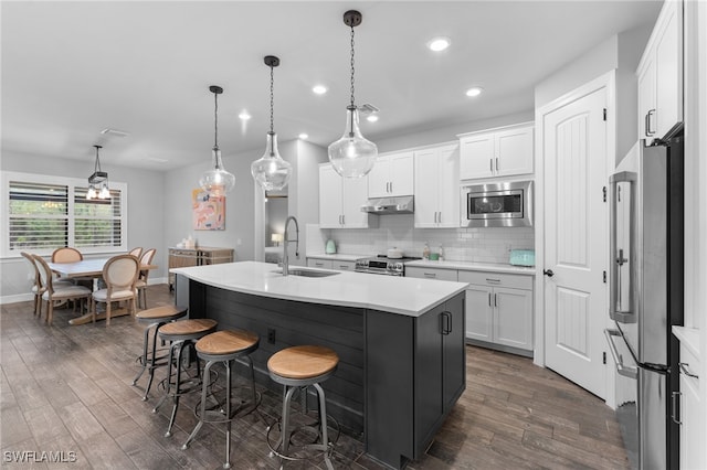 kitchen featuring a kitchen island with sink, hanging light fixtures, white cabinets, and appliances with stainless steel finishes