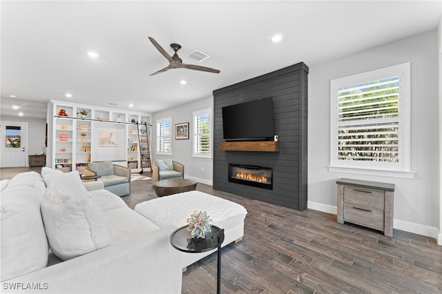 living room featuring ceiling fan, a large fireplace, and dark hardwood / wood-style floors