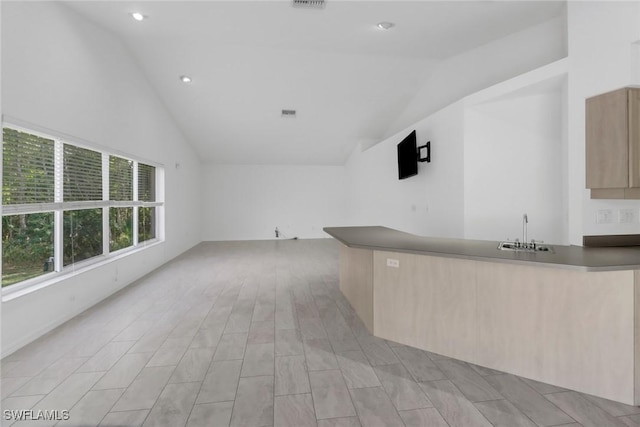 bar with light brown cabinetry, sink, and lofted ceiling