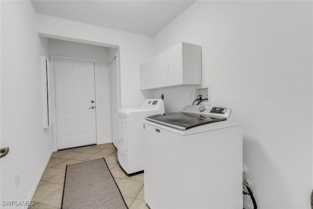 clothes washing area featuring cabinets, washing machine and clothes dryer, and light tile patterned floors