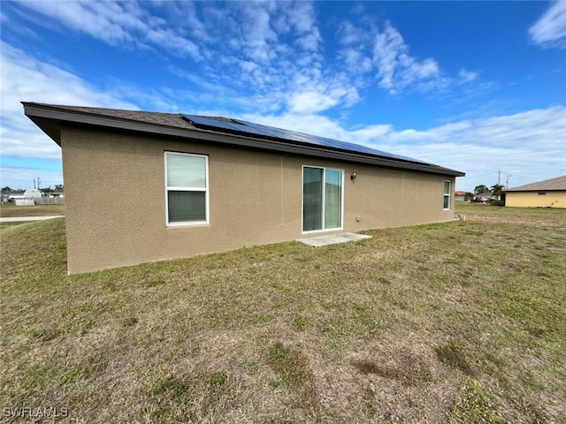 rear view of house featuring a yard and solar panels