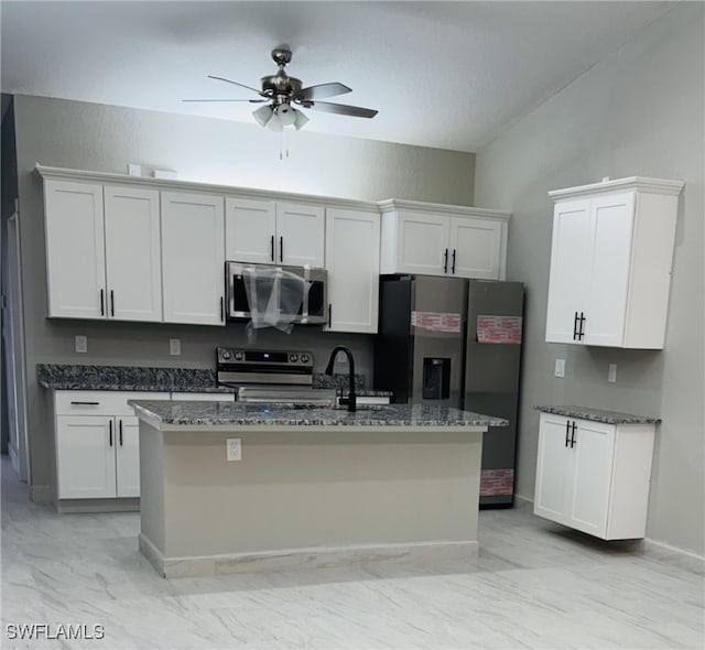 kitchen with dark stone counters, stainless steel appliances, marble finish floor, white cabinetry, and a kitchen island with sink