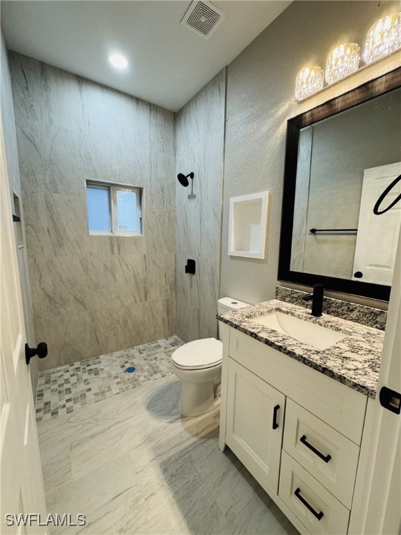 bathroom featuring visible vents, toilet, marble finish floor, tiled shower, and vanity