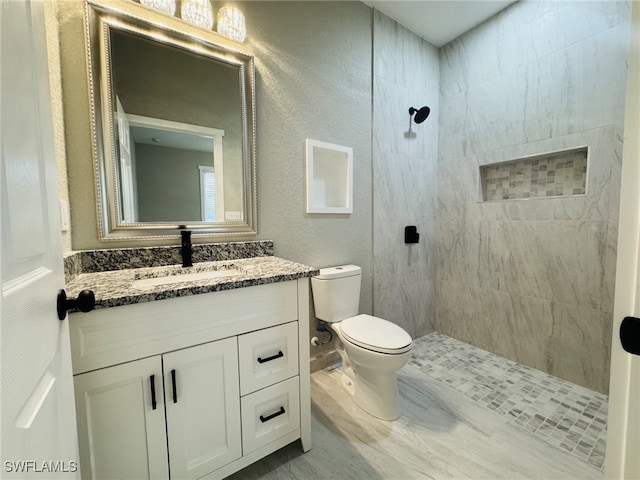 full bath with vanity, toilet, a textured wall, and a tile shower