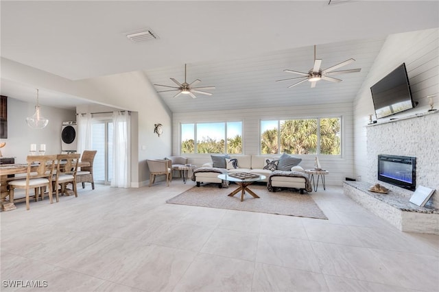 living area with visible vents, a stone fireplace, stacked washer and clothes dryer, and a healthy amount of sunlight