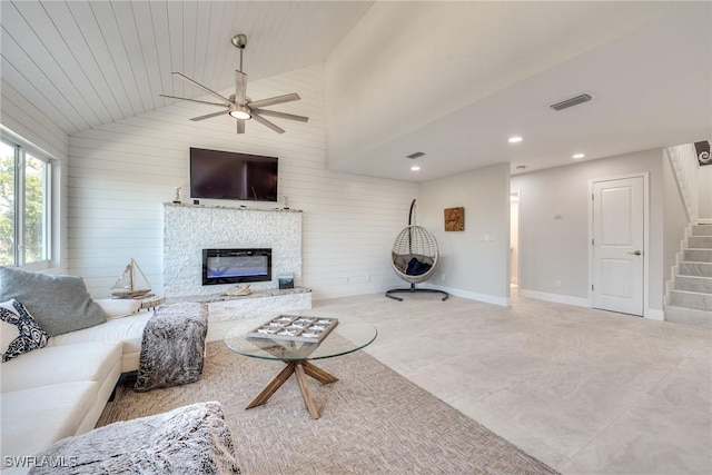 living area with lofted ceiling, visible vents, a glass covered fireplace, wood walls, and stairs