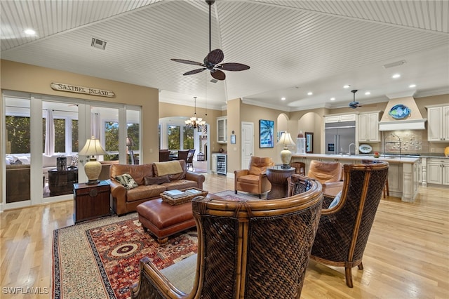 living room with ornamental molding, ceiling fan with notable chandelier, and light hardwood / wood-style flooring