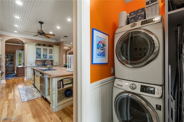 clothes washing area featuring stacked washing maching and dryer, sink, ornamental molding, ceiling fan, and light hardwood / wood-style flooring