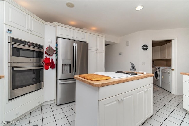 kitchen with light tile patterned flooring, washer and dryer, appliances with stainless steel finishes, a kitchen island, and white cabinets