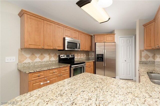 kitchen featuring appliances with stainless steel finishes, a sink, backsplash, and light stone counters