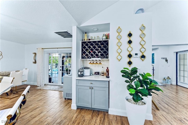 bar with gray cabinets, vaulted ceiling, a textured ceiling, and light hardwood / wood-style flooring