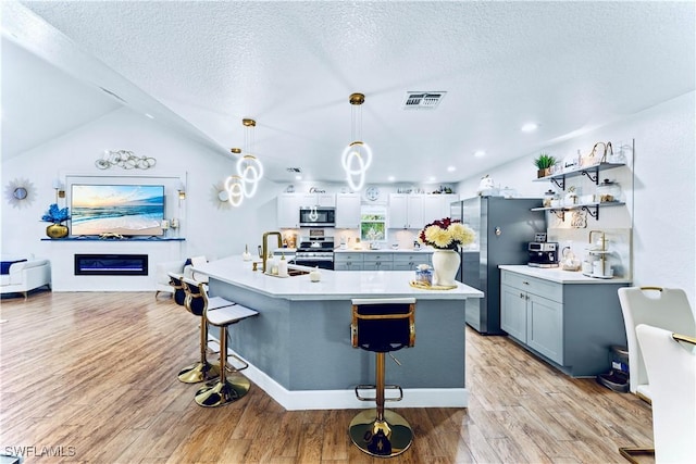 kitchen featuring sink, appliances with stainless steel finishes, a kitchen breakfast bar, decorative light fixtures, and light wood-type flooring