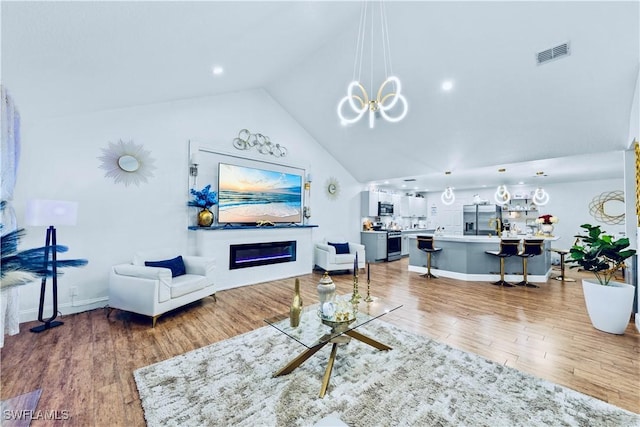 living room featuring an inviting chandelier, wood-type flooring, and high vaulted ceiling