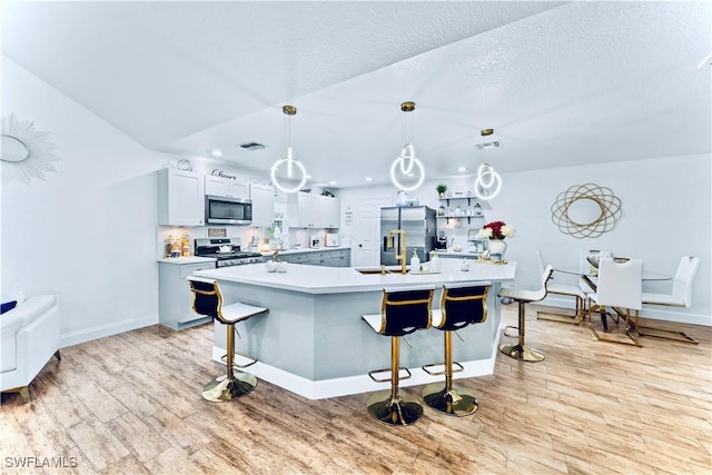 kitchen with hanging light fixtures, appliances with stainless steel finishes, a kitchen island with sink, and a kitchen breakfast bar