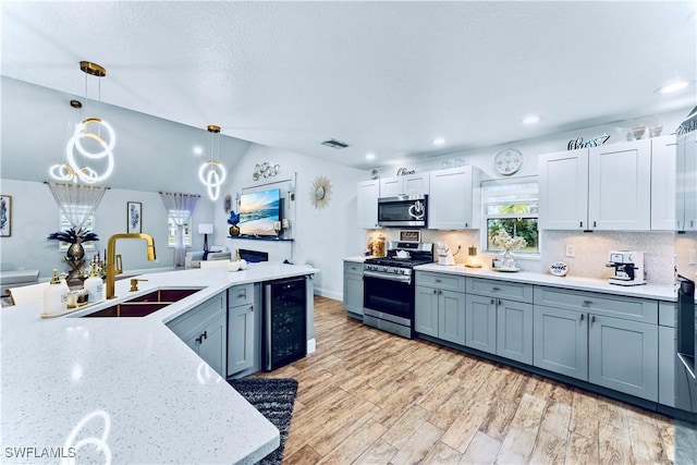 kitchen featuring appliances with stainless steel finishes, sink, beverage cooler, hanging light fixtures, and light wood-type flooring