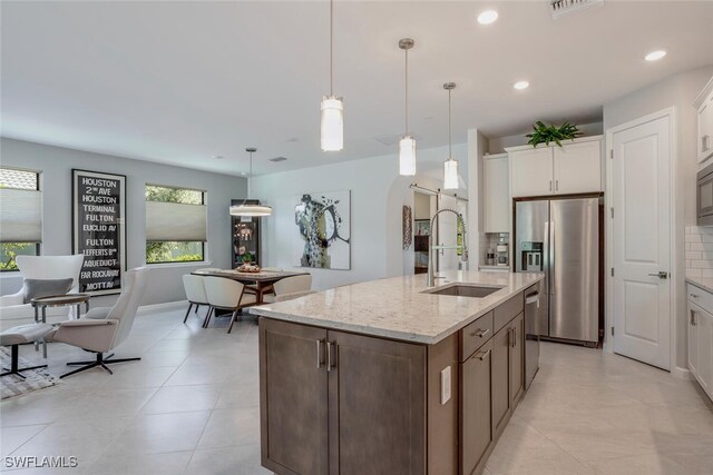 kitchen featuring sink, appliances with stainless steel finishes, white cabinetry, an island with sink, and decorative light fixtures