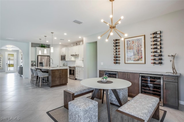 dining space featuring wine cooler, sink, light tile patterned floors, and a notable chandelier