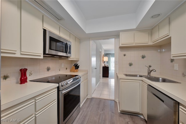 kitchen with sink, light wood-type flooring, stainless steel appliances, cream cabinets, and backsplash