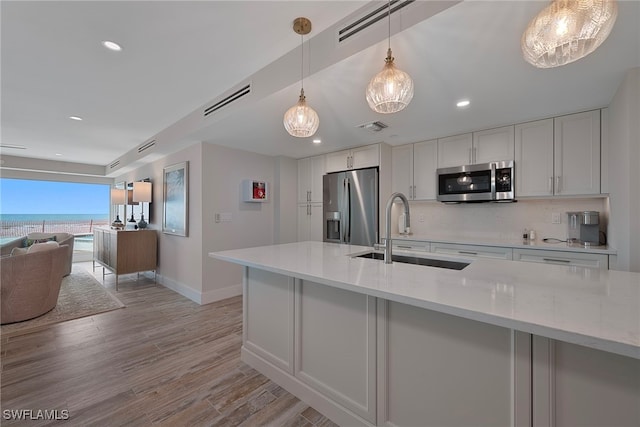 kitchen with sink, white cabinetry, hanging light fixtures, stainless steel appliances, and light stone counters