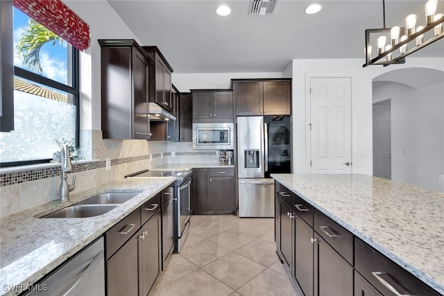 kitchen with stainless steel appliances, light stone countertops, sink, and pendant lighting