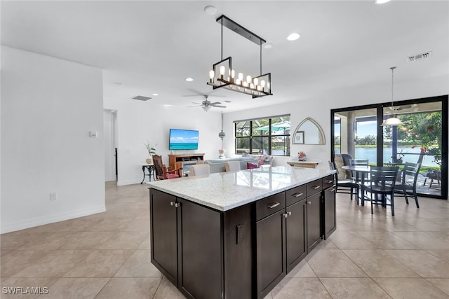 kitchen featuring dark brown cabinetry, hanging light fixtures, light tile patterned floors, a kitchen island, and light stone countertops