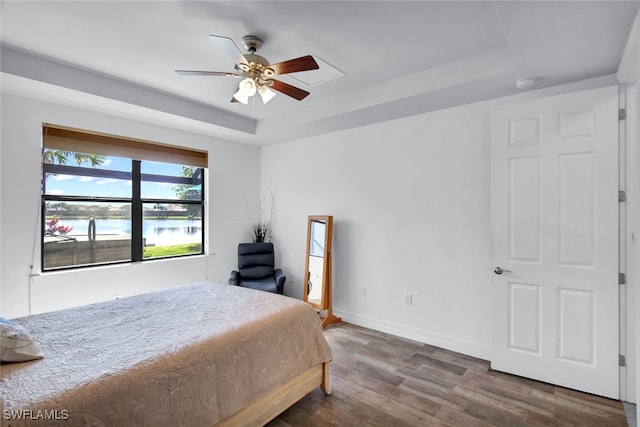 bedroom featuring a tray ceiling, dark wood-type flooring, ceiling fan, and a water view