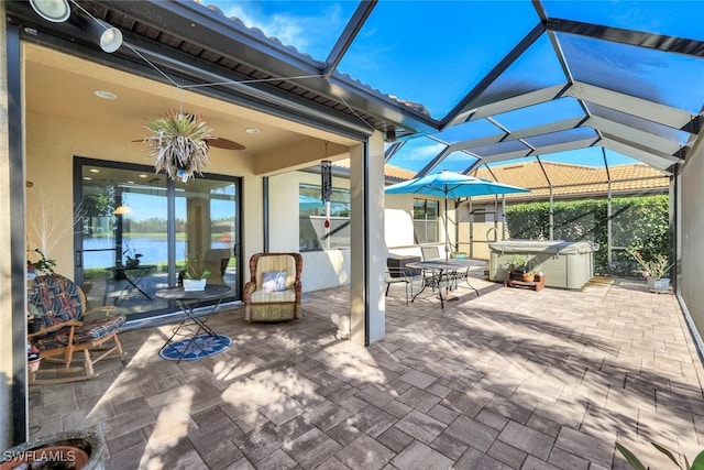 view of patio with ceiling fan, a hot tub, and glass enclosure