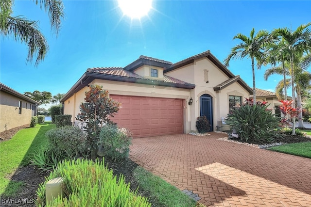 mediterranean / spanish-style house with a garage, decorative driveway, a tiled roof, and stucco siding