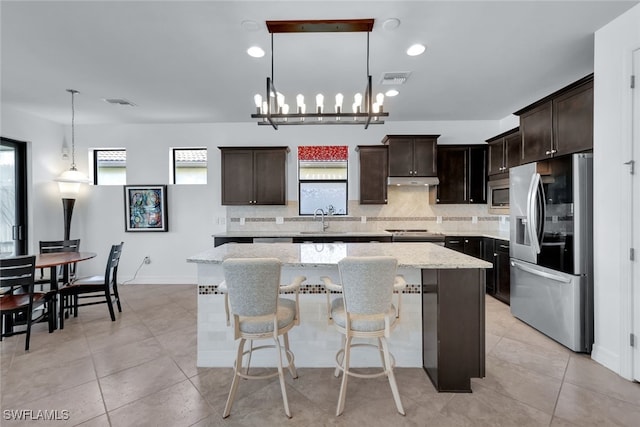 kitchen featuring appliances with stainless steel finishes, a center island, dark brown cabinets, and decorative backsplash