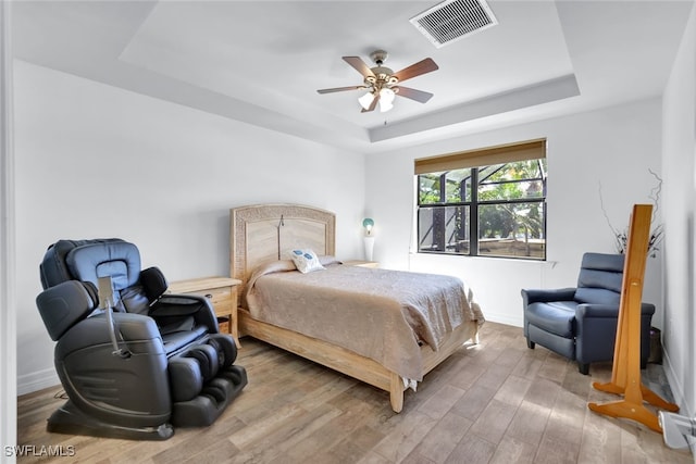 bedroom with baseboards, visible vents, a tray ceiling, and wood finished floors