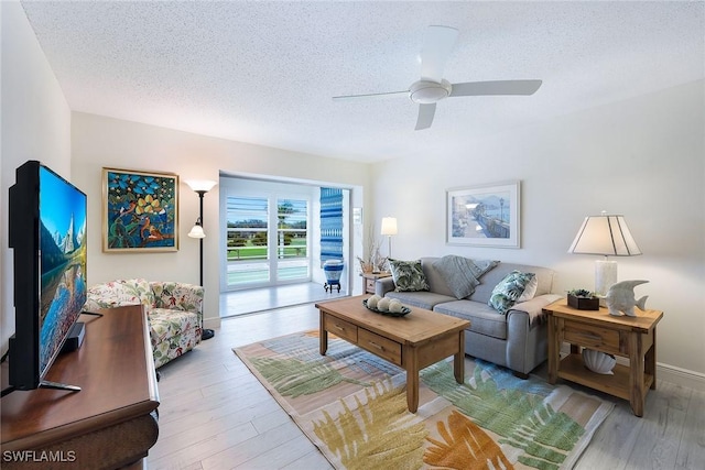 living room featuring ceiling fan, a textured ceiling, and light wood-type flooring