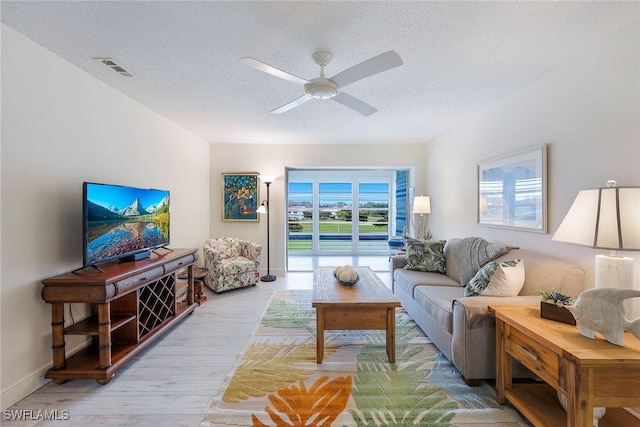 living room with ceiling fan, a textured ceiling, and light hardwood / wood-style flooring