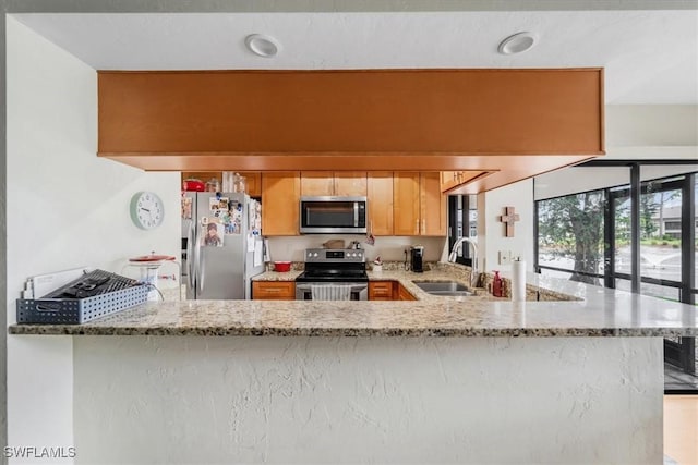 kitchen featuring sink, light stone countertops, kitchen peninsula, and appliances with stainless steel finishes