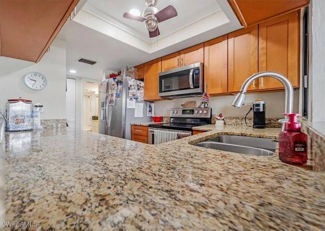 kitchen featuring sink, ceiling fan, appliances with stainless steel finishes, a tray ceiling, and light stone countertops