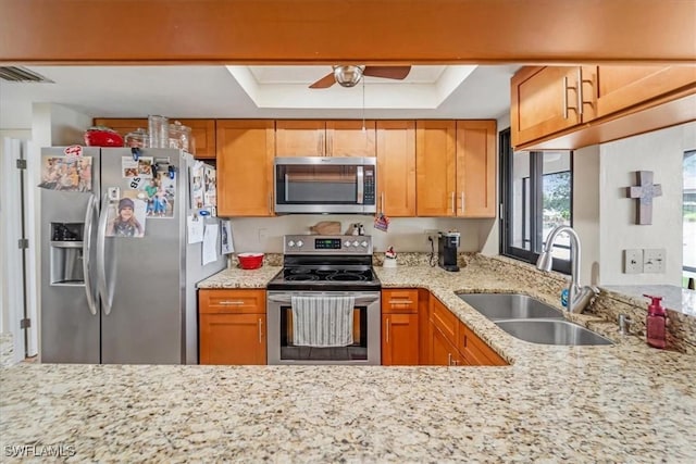 kitchen with appliances with stainless steel finishes, a raised ceiling, sink, and light stone countertops