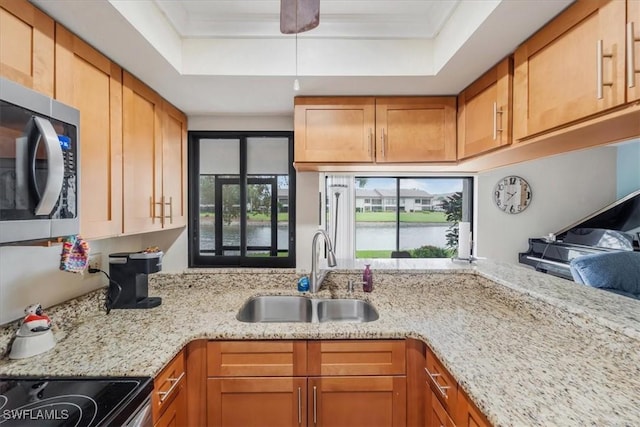 kitchen featuring a raised ceiling, light stone countertops, sink, and a water view