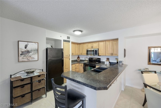 kitchen featuring dark countertops, light tile patterned floors, a peninsula, black appliances, and a sink